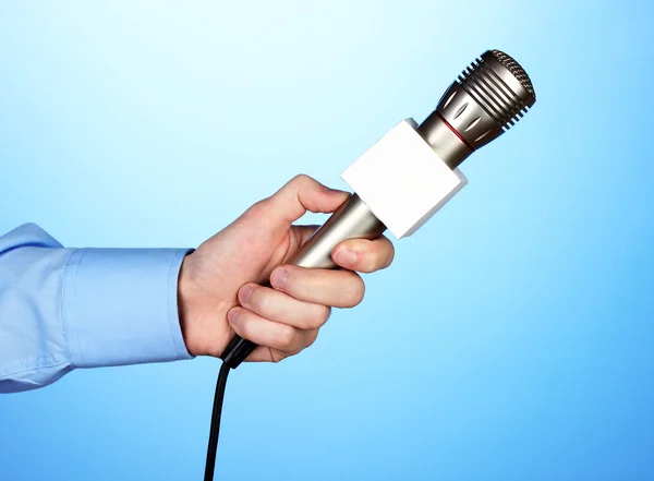 Mão masculina com microfone no fundo azul — Fotografia de Stock