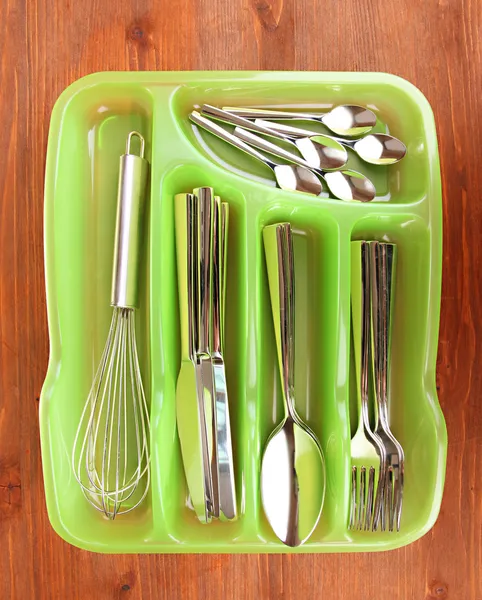 Green plastic cutlery tray with checked cutlery on wooden table — Stock Photo, Image