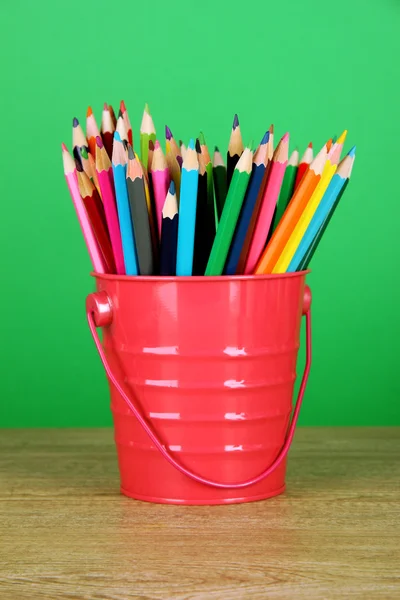 Kleurrijke potloden in emmer op tafel op groene achtergrond — Stockfoto