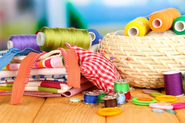 Wicker basket with accessories for needlework on wooden table, on bright background — Stock Photo, Image