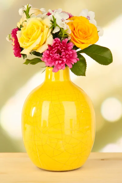 Beau bouquet de fleurs lumineuses en vase de couleur, sur table en bois, sur fond lumineux — Photo