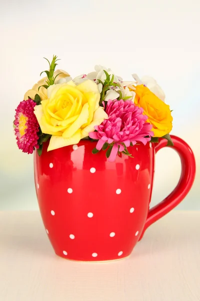 Hermoso ramo de flores brillantes en taza de color, sobre mesa de madera, sobre fondo brillante —  Fotos de Stock