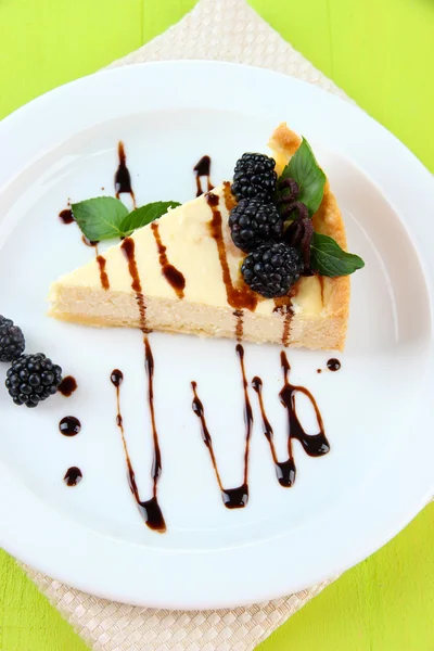 Rebanada de pastel de queso con salsa de chocolate y mora en el plato, sobre fondo de madera — Foto de Stock