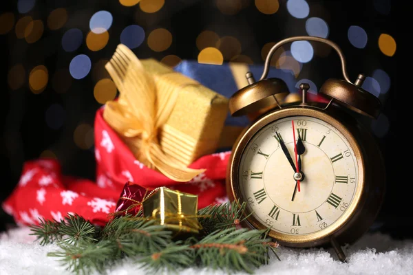 Reloj despertador con nieve y regalos en la mesa sobre fondo brillante —  Fotos de Stock