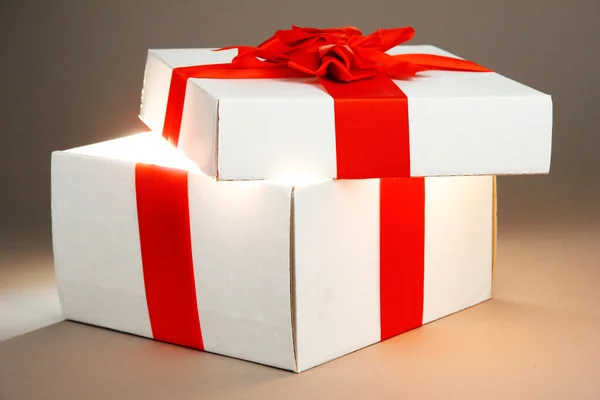 Geschenkbox mit hellem Licht auf grauem Hintergrund — Stockfoto