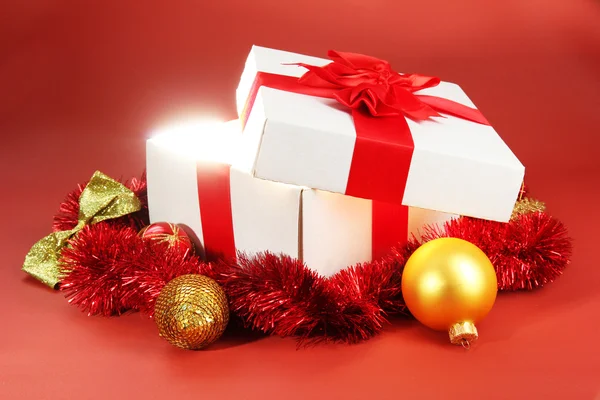 Gift box with bright light on it on red background — Stock Photo, Image