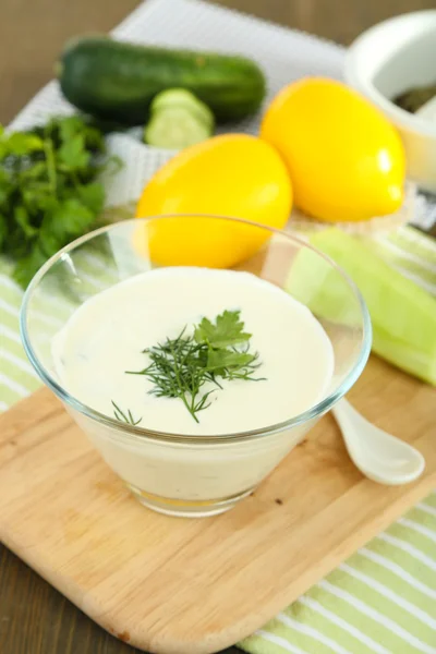 Komkommer yoghurt in glazen kom, op kleur servet, op houten achtergrond — Stockfoto