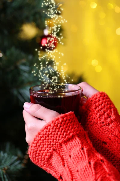 Hände halten Becher mit Heißgetränk, Nahaufnahme, auf dem Hintergrund des Weihnachtsbaums — Stockfoto