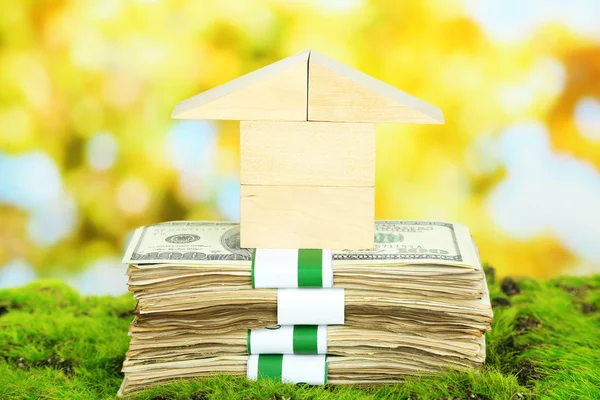Wooden house on packs of dollars on grass on natural background — Stock Photo, Image