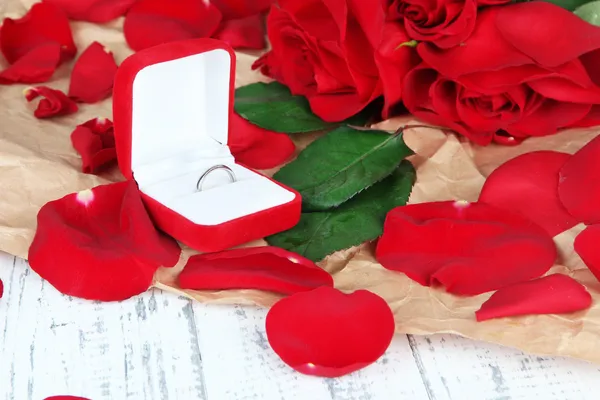 Ring umgeben von Rosen und Blütenblättern auf Holztisch in Großaufnahme — Stockfoto