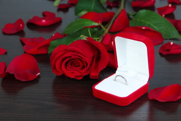 Ring surrounded by roses and petals on wooden table close-up — Stock Photo, Image