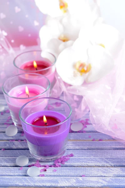 Hermosas velas de colores y flores de orquídea, sobre mesa de madera de color, sobre fondo claro — Foto de Stock