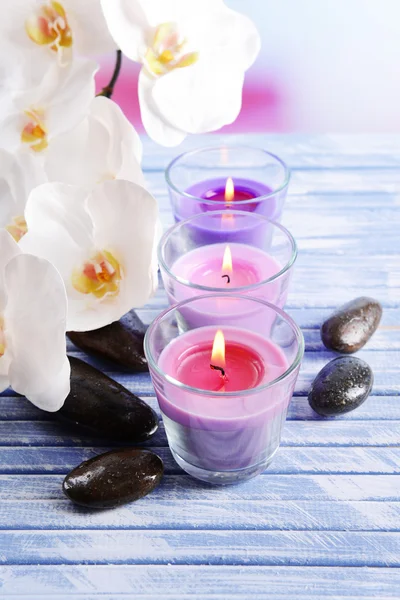 Hermosas velas de colores, piedras de spa y flor de orquídea, sobre mesa de madera de color, sobre fondo claro —  Fotos de Stock