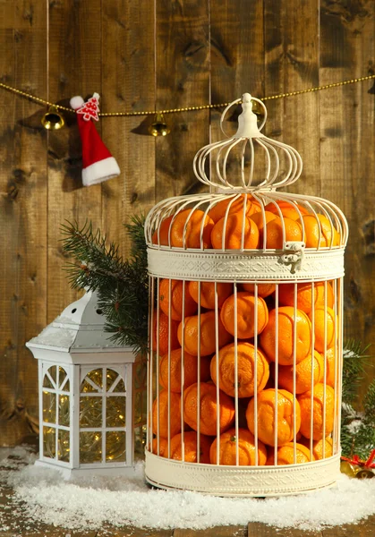 Mandarijnen in decoratieve kooi met kerst decor, op houten achtergrond — Stockfoto