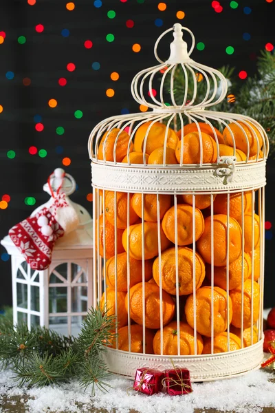 Mandarijnen in decoratieve kooi met kerst decor, op glanzende achtergrond — Stockfoto