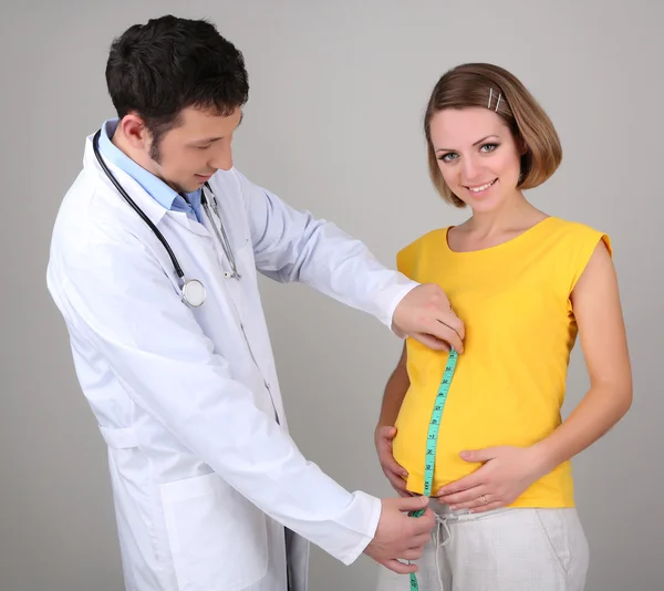 Młoda kobieta w ciąży z lekarzem na szarym tle — Zdjęcie stockowe