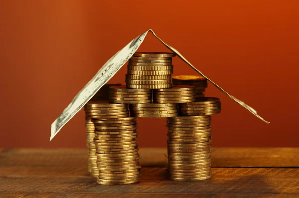 Coins house on table on brown background Royalty Free Stock Photos