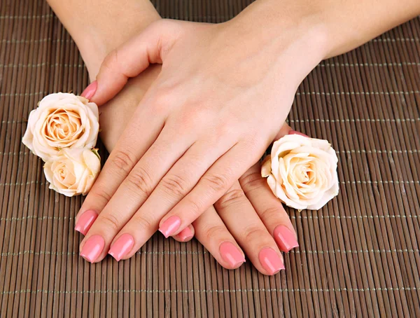 Mãos de mulher com manicure rosa e flores, em fundo tapete de bambu — Fotografia de Stock