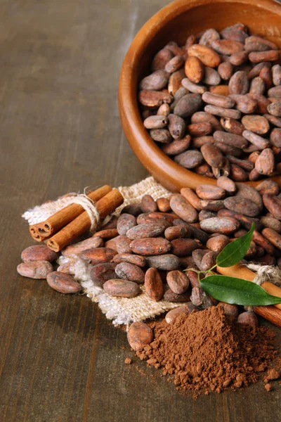 Какао бобы в миске, какао порошок и специи на деревянном фоне — стоковое фото