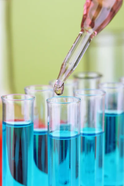 Pipeta de laboratorio con gota de líquido de color sobre tubos de ensayo de vidrio, primer plano — Foto de Stock