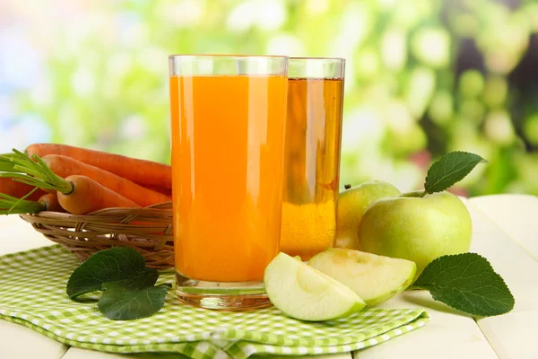 Glazen van SAP, appelen en wortelen op witte houten tafel, op groene achtergrond — Stockfoto