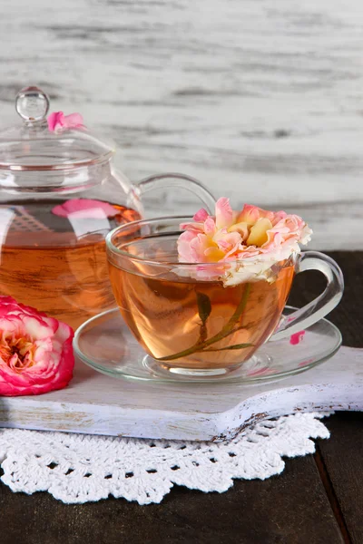 Vattenkokare och kopp te från tea rose ombord på servett på träbord på trä bakgrund — Stockfoto