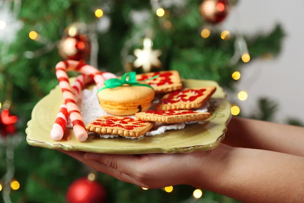 Mãos segurando prato com biscoitos caseiros e doces, em fundo brilhante — Fotografia de Stock