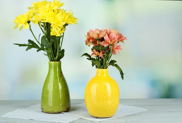 Beautiful flowers in vases, on wooden table, on light background — Stock Photo, Image