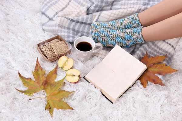 Composición con cuadros calientes, libro, taza de bebida caliente y piernas femeninas, sobre fondo de alfombra de color — Foto de Stock