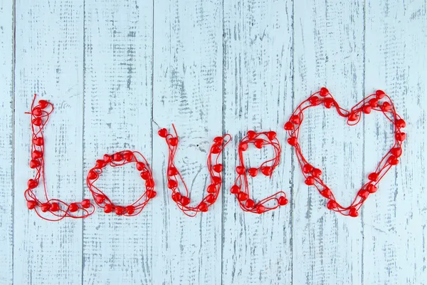 Heart-shaped beads on string on wooden background — Stock Photo, Image