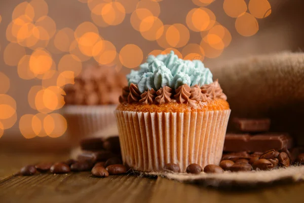 Sabrosos cupcakes con crema de mantequilla, sobre mesa de madera, sobre fondo de luces —  Fotos de Stock