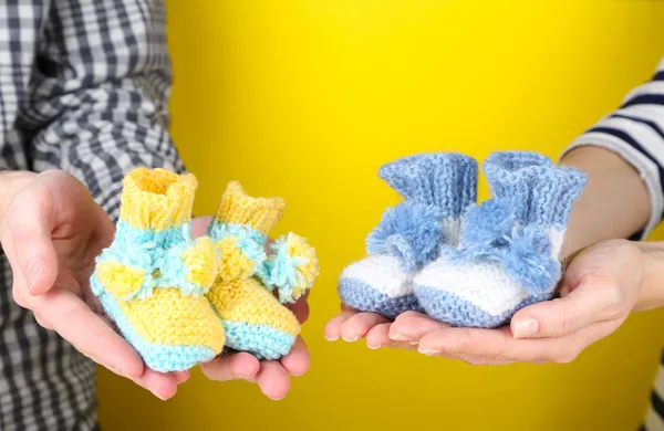 Hands with crocheted booties for baby, on color background — Stock Photo, Image