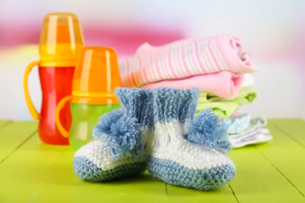 Composition with crocheted booties for baby,clothes, bottles on wooden background — Stock Photo, Image