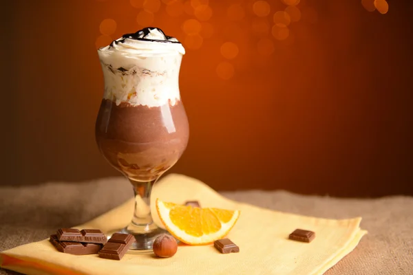 Sabroso postre con chocolate, crema y salsa de naranja, sobre mesa de madera, sobre fondo de luces — Foto de Stock