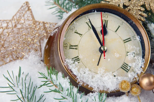 Часы с еловыми ветками и рождественскими украшениями под снегом крупным планом — стоковое фото