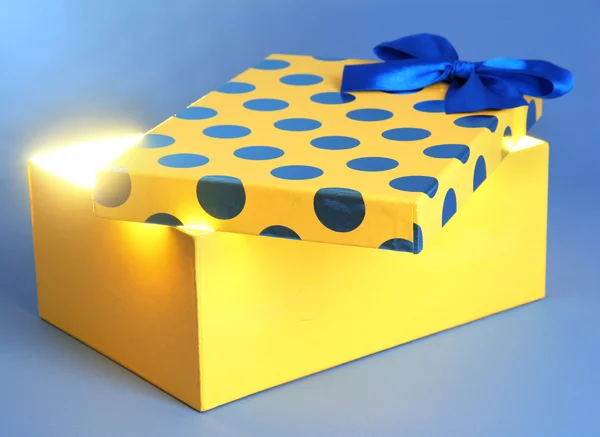 Gift box with bright light on it on blue background — Stock Photo, Image