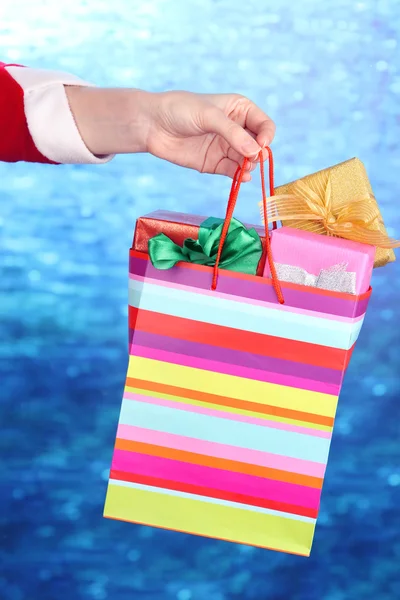 Mano tiene il pacchetto con i regali di Capodanno su sfondo blu — Foto Stock