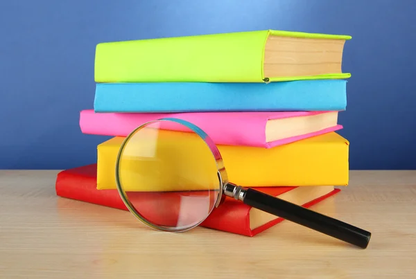 Color books with magnifying glass on table on blue background — Stock Photo, Image