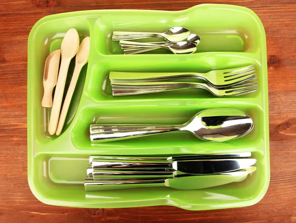 Green plastic cutlery tray with checked cutlery and wooden spoons on wooden table — Stock Photo, Image