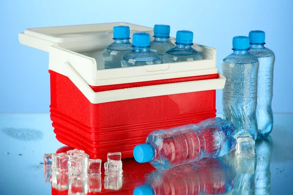 Reizende koelkast met flessen water en ijsblokjes, op blauwe achtergrond — Stockfoto