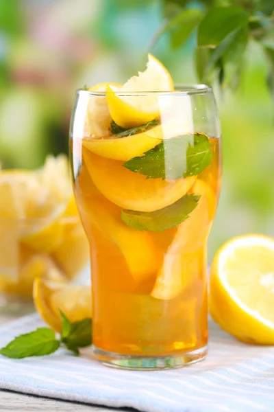 Холодный чай с лимоном и мятой на деревянном столе, на открытом воздухе — стоковое фото