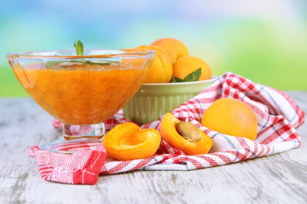 Marillenmarmelade in Glasschale und frischen Aprikosen, auf Holztisch, auf hellem Hintergrund — Stockfoto