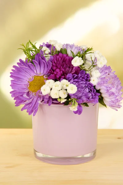 Beautiful bouquet of bright flowers in glass vase, on wooden table, on bright background — Stock Photo, Image