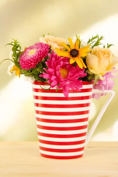 Belo buquê de flores brilhantes na caneca a cores, na mesa de madeira, no fundo brilhante — Fotografia de Stock