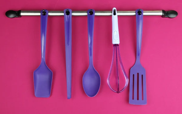 Plastic kitchen utensils on silver hooks on red background — Stock Photo, Image