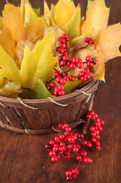 Schöne Herbstblätter und rote Beeren im Korb auf hölzernem Hintergrund — Stockfoto