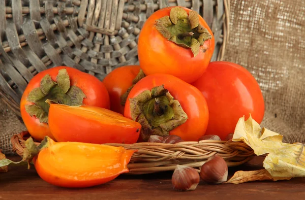 Ripe persimmons with nuts on table on wicker background — Stock Photo, Image