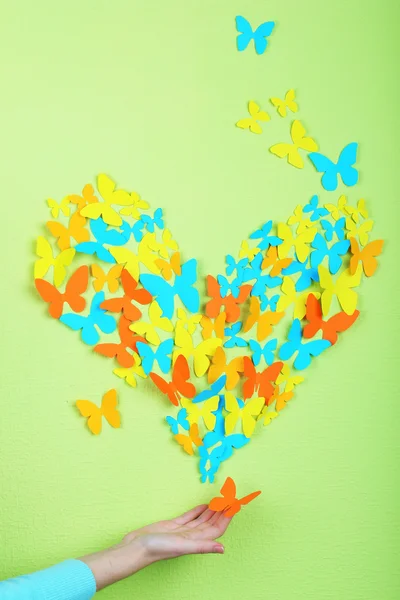 Paper butterflies on hand on green wall background — Stock Photo, Image