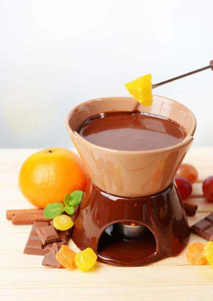 Chocolade fondue met fruit, op houten tafel, op lichte achtergrond — Stockfoto