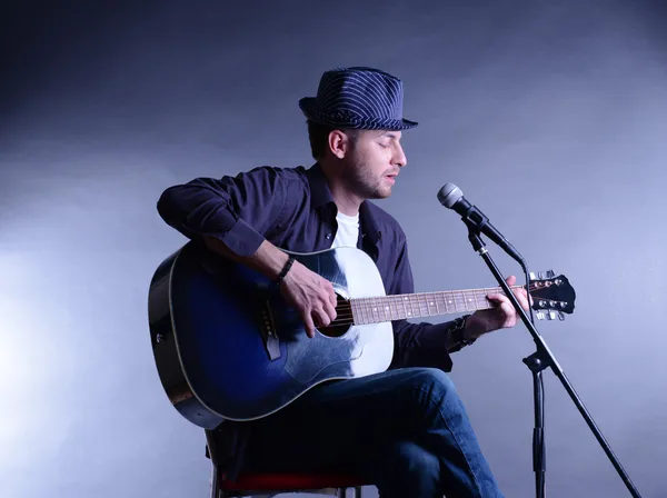 Giovane musicista che suona la chitarra acustica e canta, su sfondo grigio — Foto Stock